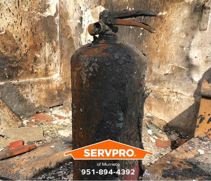 A burnt fire extinguisher sits in a fire-damaged room.