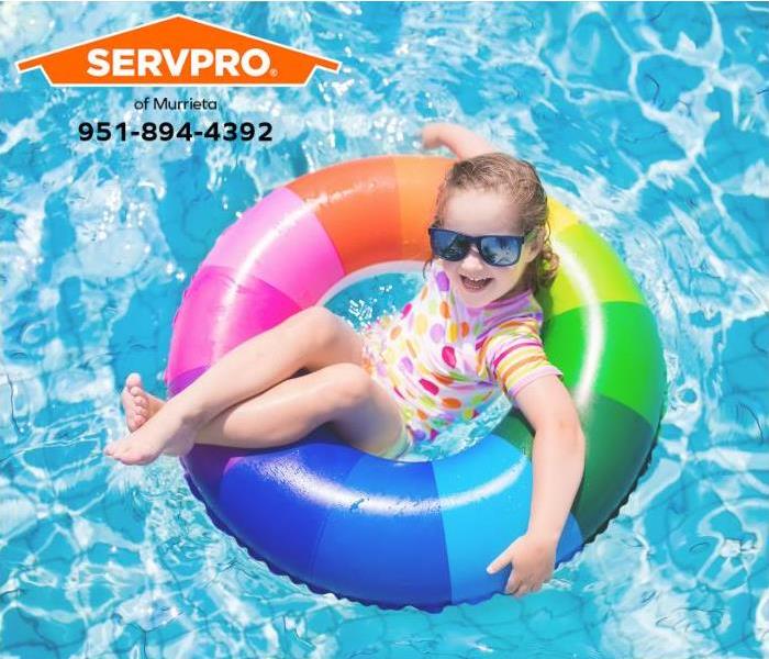 A child is floating in a swimming pool in a colorful inflatable ring.