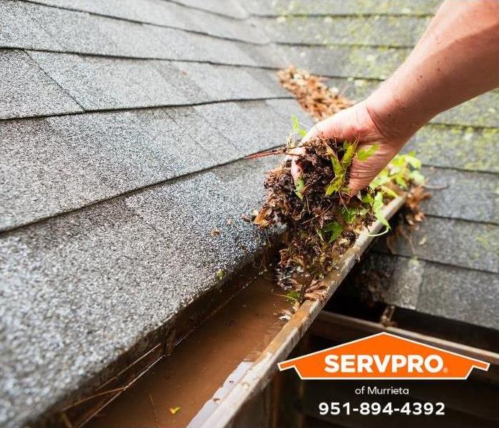 A person clears debris from a clogged rain gutter.