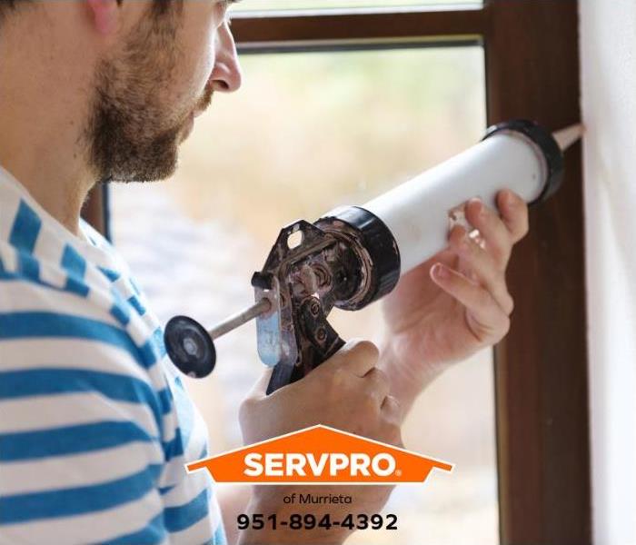 A person is caulking a leaking window to prevent water intrusion.