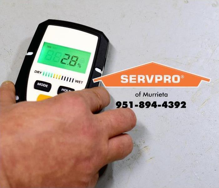 A SERVPRO technician is shown using a moisture detection device to measure moisture in a room. 
