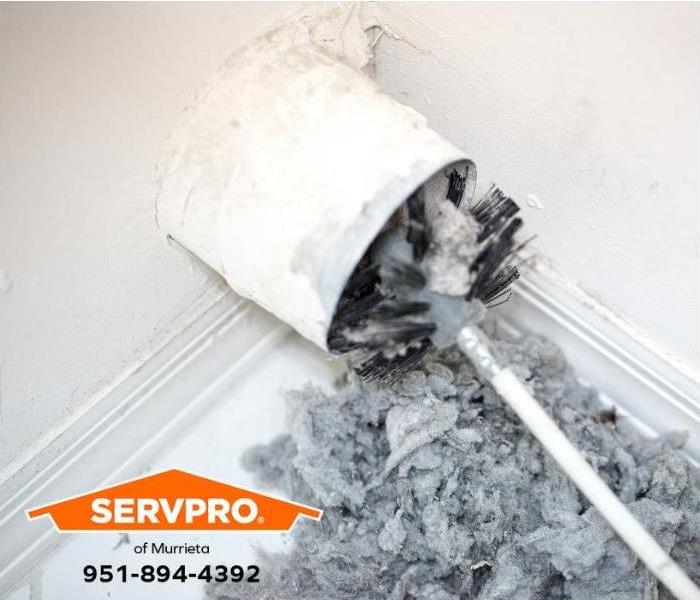 A clogged dryer vent is being cleaned with a round brush.